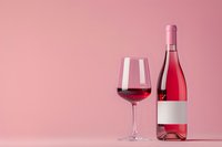 Glass of rose wine and bottle with blank label on pink background, minimalist composition for wine marketing and promotion materials.