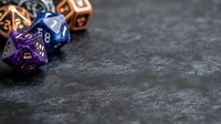 Colorful polyhedral dice for tabletop gaming scattered on dark textured surface with copy space, featuring purple, blue and orange colors. Gaming concept.