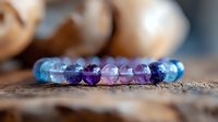 Colorful gemstone bracelet with purple amethyst, rose quartz and blue topaz beads arranged in gradient pattern on rustic wooden surface, macro jewelry photography.