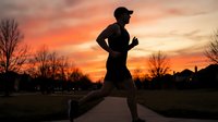 Silhouette of male runner jogging on wooden path during golden sunset with bare trees, outdoor fitness and endurance training.