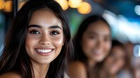 Young Asian woman with bright authentic smile and natural makeup against blurred bokeh lights background, expressing joy and confidence.
