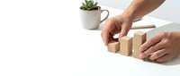 Male hands arranging wooden blocks in ascending order on white desk with succulent plant, representing business growth and strategic planning.