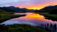 Tranquil mountain lake at sunset with vibrant orange and pink sky reflecting on calm water surface surrounded by green hills and grassland creating peaceful scenery.