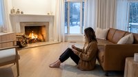 Young woman relaxing by fireplace in cozy living room reading book on tablet device. Modern home interior with warm lighting for lifestyle content.