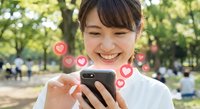 Happy young Asian woman using smartphone with floating heart icons in sunny park, social media engagement and digital communication concept.