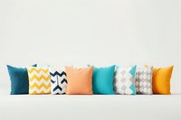 Decorative throw pillows arranged in row featuring modern geometric patterns and solid colors in teal, yellow, peach and gray on white background.