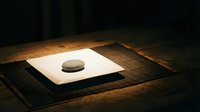 Minimalist stone on white paper placed on wooden surface with warm ambient lighting, suitable for zen meditation, wellness, and contemporary design projects.