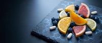 Fresh citrus fruits and berries arranged on dark slate board with ice cubes for healthy nutrition and vitamin supplements concept.