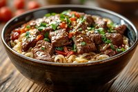Tender beef chunks with noodles in savory sauce garnished with fresh herbs and cherry tomatoes served in rustic brown ceramic bowl on wooden table.