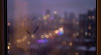 Heart drawn on foggy window glass with blurred city lights bokeh background creating romantic atmosphere for Valentine's Day and love concepts.