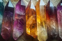 Colorful crystal quartz points in purple, orange, and yellow hues arranged in row formation showing natural mineral structure and healing stone properties.