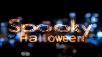 Light painted text spelling "Spooky Halloween" glows against dark background with blue bokeh lights, creating magical nighttime atmosphere for seasonal design.