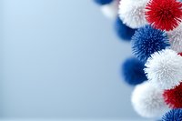 Festive red, white and blue pom pom decorations creating patriotic border against light blue background, suitable for holiday celebrations and party designs.