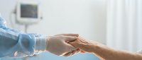 Healthcare professional in blue scrubs holding elderly patient hand providing comfort and support in modern medical facility.