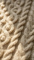 Close-up of beige cable knit wool sweater texture showing intricate braided pattern and soft yarn fibers for cozy winter fashion and textile design.