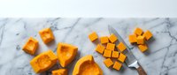 Fresh orange butternut squash cubes and slices on marble surface with knife for healthy cooking and meal preparation.