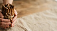 Hands holding bundle of cinnamon sticks tied with twine on wooden surface. Spice ingredient for cooking, baking, and culinary use.