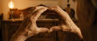 Elderly hands forming a heart shape in warm vintage interior light, symbolizing love, care, and lifelong devotion in a cozy home setting.