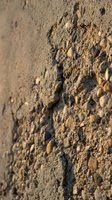 Rough textured concrete wall surface with embedded stones and pebbles creating natural weathered pattern for construction and architectural backgrounds.