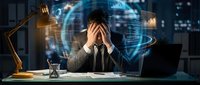 Stressed businessman holding head in hands at desk with holographic data visualization and digital interface in modern office environment at night.