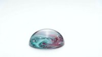 Translucent glass dome with swirling teal and pink colors creating marble effect on white background for design projects and creative applications.