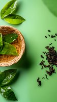 Fresh green tea leaves in woven bamboo basket with scattered dry black tea on green background. Minimalist food composition with copy space for wellness design.