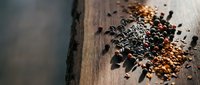 Assorted spices and seeds scattered on rustic wooden surface creating aromatic culinary ingredient display for cooking and food preparation backgrounds.