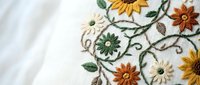 Delicate floral embroidery on white fabric featuring colorful daisies and leaves in traditional needlework style for textile and craft projects.