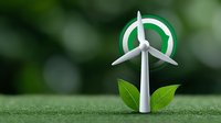 Wind turbine model with green leaves on grass surface against blurred natural background, representing renewable energy and environmental sustainability.