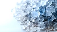 Macro view of crystalline sea salt flakes showing transparent and blue-tinted crystals with detailed mineral structure against white background. Culinary and spa concept.