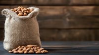 Raw almonds spilling from rustic burlap sack on dark wooden table background, natural healthy nuts in vintage setting for food photography.