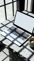 Laptop with blank white screen on stone surface outdoors, coffee cup beside it, sunlight casting grid shadows. Remote work mockup.
