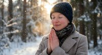 Peaceful young woman meditating outdoors in snowy winter forest with warm sunlight, practicing mindfulness and gratitude in serene natural setting.