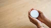 Hand holding white round object on wooden surface background for product display and mockup purposes.