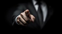 Businessman in dark suit pointing finger directly at viewer, dramatic low-key lighting creating professional atmosphere for leadership or recruitment concept.