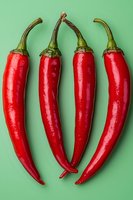 Fresh red chili peppers arranged in row on mint green background. Vibrant food photography showing glossy texture and curved shapes of spicy cayenne peppers.