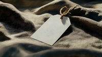 Blank white paper tag with twine string on soft fabric background in moody lighting. Mockup for branding and product labeling.