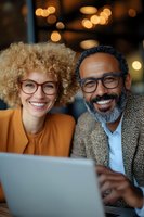 Diverse business colleagues with glasses working together on laptop in cafe with warm bokeh lighting. Casual professional meeting atmosphere.