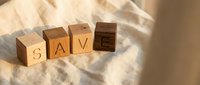 Wooden letter cubes spelling SAVE on a soft linen fabric background in warm natural light, symbolizing financial savings and budgeting concepts.