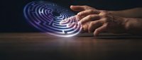 Hand holding glowing neon spiral disc with blue and purple light trails on dark surface, representing technology, innovation, and digital transformation concepts.