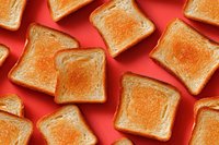 Golden toasted bread slices arranged on vibrant coral background, creating contrast between crispy texture and smooth surface for food advertising.