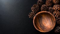 Rustic wooden bowl with natural pine cones arranged on dark background. Minimalist winter holiday composition with organic elements and warm tones.