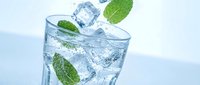 Refreshing sparkling water with ice cubes and fresh mint leaves splashing in clear glass against light blue background for summer beverage concepts.