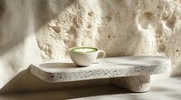 Minimalist matcha latte in white ceramic cup on modern concrete shelf against textured wall with dramatic natural lighting and soft shadows.