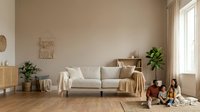 Neutral beige living room with comfortable sofa, wooden furniture, potted plants, and natural light from window. Interior design for home decor, furniture retail, and lifestyle content.