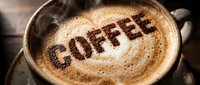 Steaming hot latte art with the word coffee written in cocoa powder on creamy froth, served in a rustic ceramic cup on a wooden table.