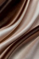 Smooth flowing brown satin fabric with elegant folds and waves creating a luxurious textile background pattern with light and shadow effects.