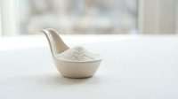 Ceramic bowl shaped like a bird filled with white powder, flour or salt on white surface with blurred background for kitchen and cooking concepts.