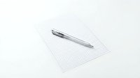 Silver ballpoint pen lying on graph paper sheet against white background for office and educational projects.