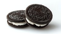 Chocolate sandwich cookies with cream filling on white background, close-up view of two round dark cookies with ornate pattern design and vanilla cream center.